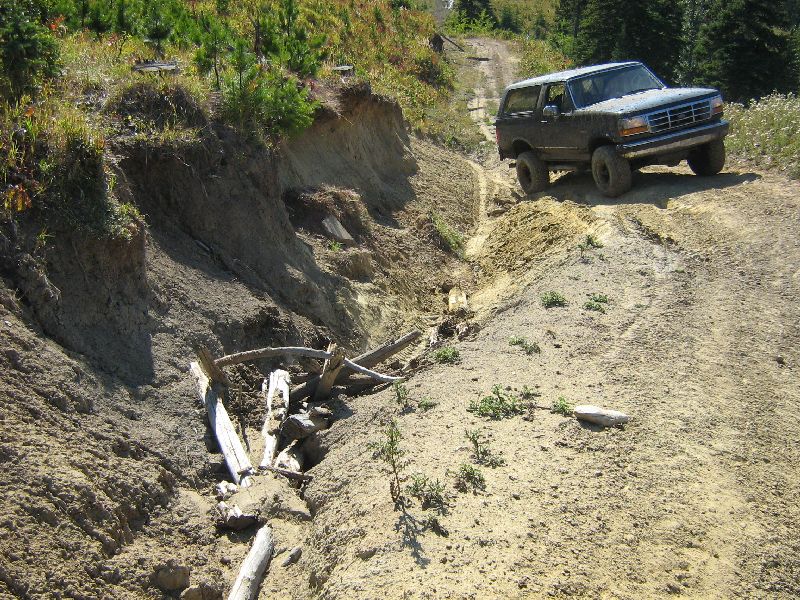 1995 Ford Bronco driving up a steep dirt road next to a washed-out embankment