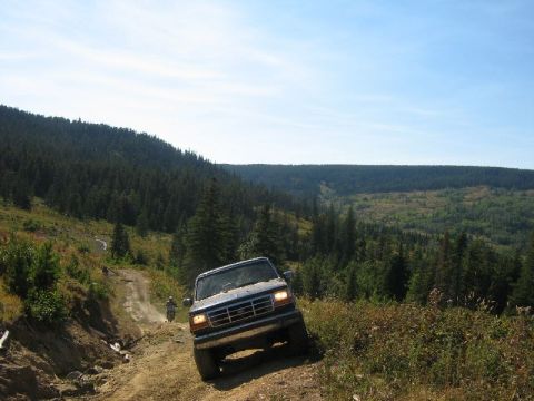 1995 Ford Bronco - A Ford Bronco navigates a steep, dusty trail through a wooded mountain landscape.