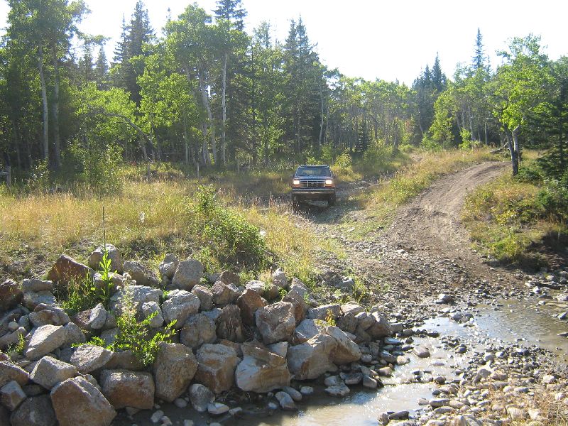Red Ford Bronco driving on a dirt path near a stream