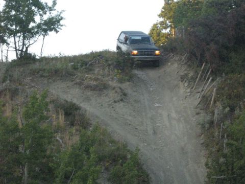 1995 Ford Bronco - A Ford Bronco navigates a challenging off-road descent on a dirt track.