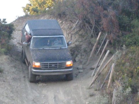 1995 Ford Bronco - A dark Ford Bronco navigates a dusty, off-road trail with wooden posts on the right.