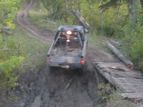1995 Ford Bronco - A pickup truck navigates a challenging muddy path with a log bridge.