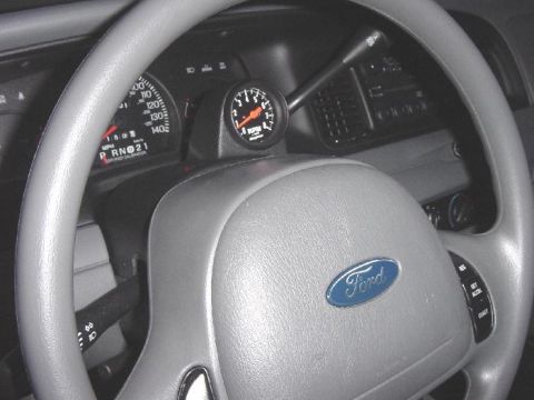 2003 Ford Crown Victoria - Close-up of a car's interior, showing the steering wheel, dashboard gauges, and an aftermarket tachometer.