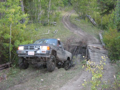 1995 Ford Bronco - Toyota pickup truck attempts to cross a muddy obstacle on an off-road trail.