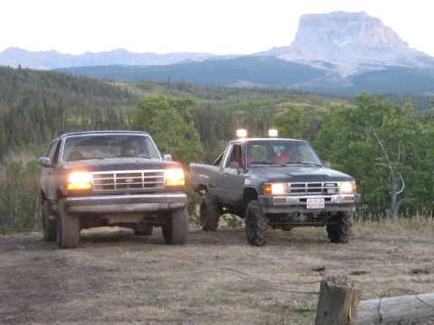 1995 Ford Bronco - A 1995 Ford Bronco is parked next to a Toyota pickup truck with a mountain range in the background.