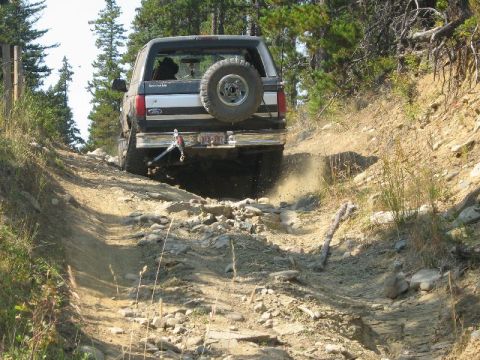 1995 Ford Bronco - Ford Bronco tackles a challenging off-road trail, kicking up dust on the rocky ascent.