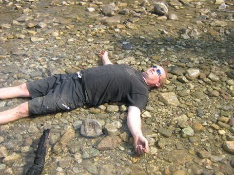 1995 Ford Bronco - A man lies on his back in a shallow, rocky stream bed.
