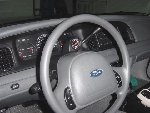 2003 Ford Crown Victoria - The dashboard and steering wheel of a car are visible, a Ford emblem and an aftermarket tachometer.