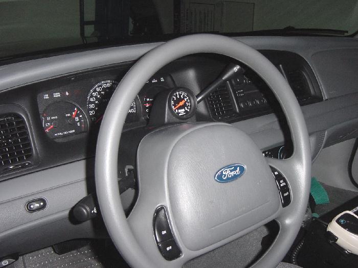 Aftermarket column-mounted tachometer pod behind the steering wheel in a gray Ford interior