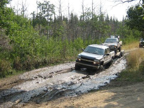 1995 Ford Bronco - Two trucks navigate a difficult muddy path, one towing the other.