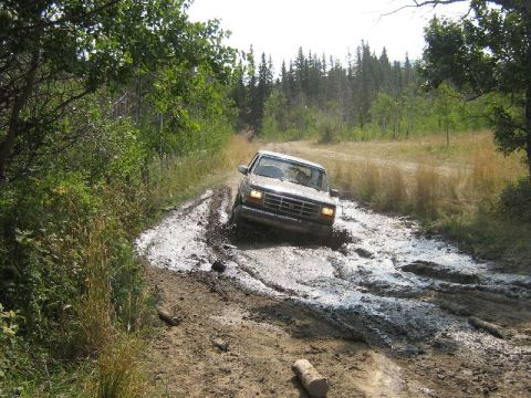 1995 Ford Bronco - A Ford Bronco navigates a challenging muddy off-road path.
