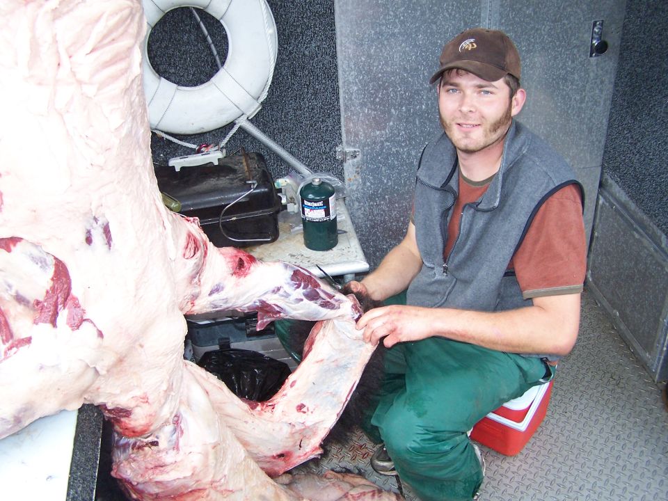 Man field-dressing a game carcass on the diamond-plate deck of a boat