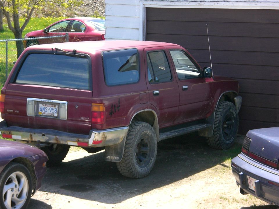Maroon Toyota 4Runner V6 4WD with lift and mud tires parked by garage, rear quarter view