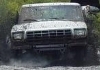 1990 Ford Bronco - White SUV navigates a muddy terrain, kicking up water and dirt.