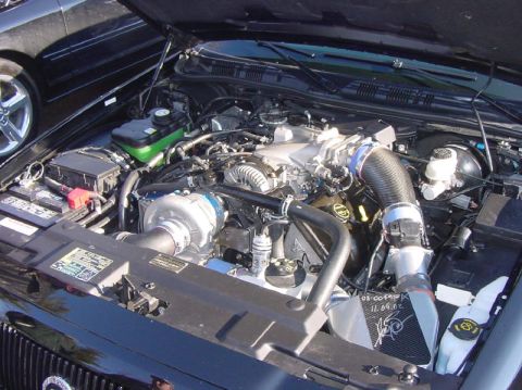 2003 Ford Crown Victoria - The engine bay of a car, a supercharger and custom intake system. Another vehicle is visible to the left.