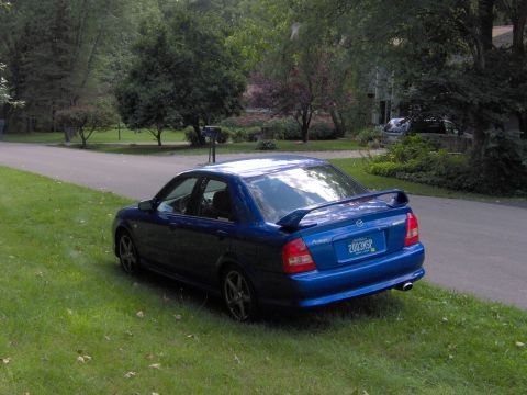 2003 Mazda Protege - Rear view of a blue 2003 Mazda Protege sedan with a spoiler, parked on the side of a road.