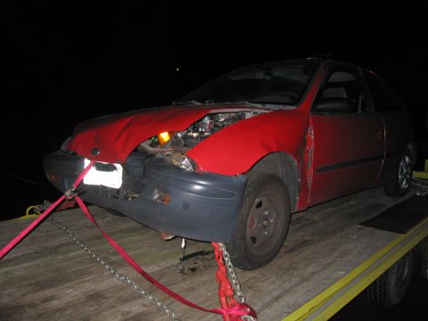 1991 Ford LTD Crown Victoria - A red hatchback with significant front-end damage is being transported on a flatbed trailer.
