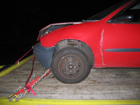 1991 Ford LTD Crown Victoria - A red car is secured with chains and straps on a yellow tow truck bed at night.