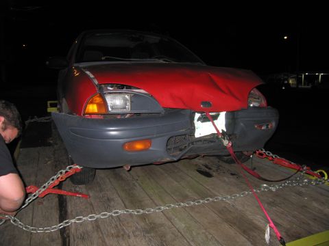 1991 Ford LTD Crown Victoria - A red car with a heavily damaged front end is secured with chains and straps for transport on a trailer.