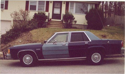 1988 Ford Crown Victoria - A 1988 Ford Crown Victoria sedan is seen from the side, parked in front of a residential building.
