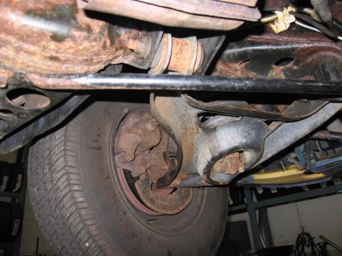 1991 Ford LTD Crown Victoria - The underside of a vehicle reveals its suspension system and a worn tire, with visible signs of rust on the metal parts.