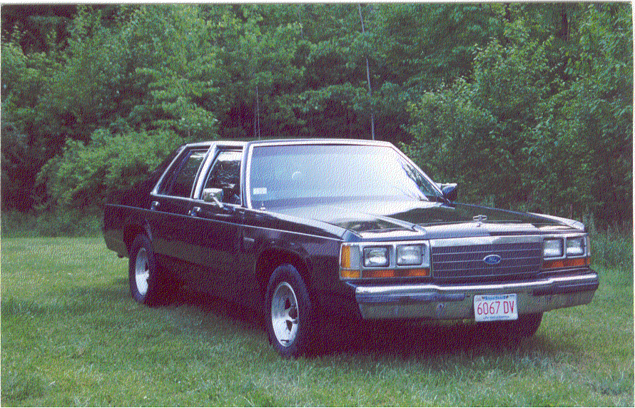 Black Ford LTD Crown Victoria sedan parked on grass, front three-quarter view