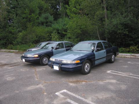 1991 Ford LTD Crown Victoria - Two police interceptors, likely from the late 90s, are parked side-by-side in an outdoor lot.
