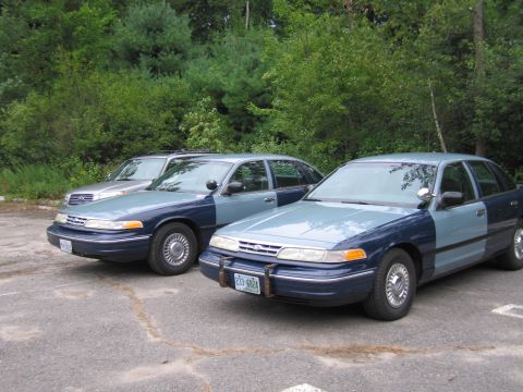 1991 Ford LTD Crown Victoria - Two Ford Crown Victoria sedans, likely police vehicles, are parked in tandem, displaying a two-tone blue and light blue paint scheme.
