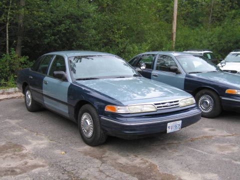 1991 Ford LTD Crown Victoria - Two Ford Crown Victorias are parked in a lot, one with a mismatched blue and light blue paint scheme.