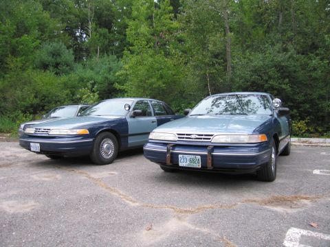 1991 Ford LTD Crown Victoria - Two Ford Crown Victoria police cars are parked in a lot, one slightly in front of the other.