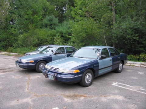 1991 Ford LTD Crown Victoria - Two police sedans, possibly Ford Crown Victorias, parked side-by-side in a lot.