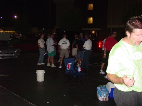 1986 Ford Mustang - A group of people stand around in a parking lot at night, with some vehicles parked nearby.