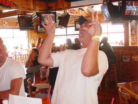 1986 Ford Mustang - A man celebrates with hand gestures inside a sports bar, with other patrons visible in the background.