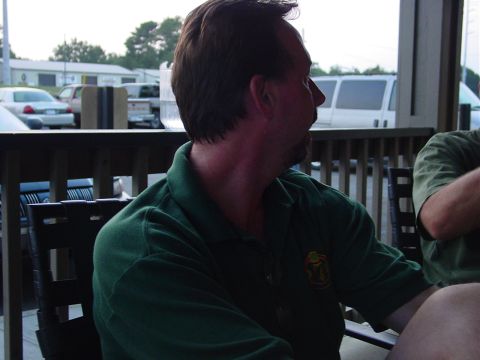 1986 Ford Mustang - A man in a green polo shirt sits at a table outdoors, with several vehicles visible in the background.