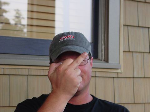1986 Ford Mustang - A man wearing a baseball cap obscures his face while giving the middle finger.