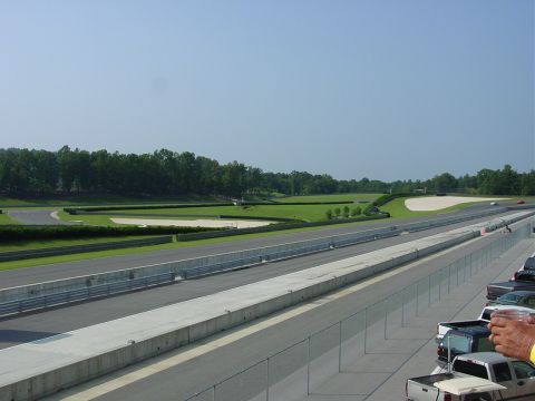1986 Ford Mustang - A view of a race track with several cars parked in the foreground under a clear blue sky.