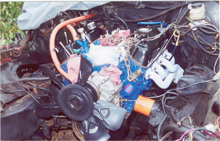 Blue V8 engine being installed in vehicle engine bay