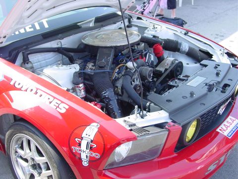 1986 Ford Mustang - The engine bay of a red race car, prominent sponsor decals and yellow headlights.
