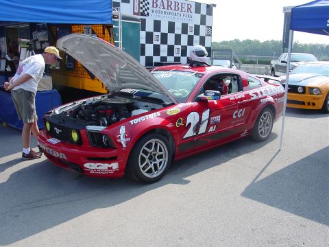 1986 Ford Mustang - A red race car with its hood open is parked next to another car at a motorsports event.