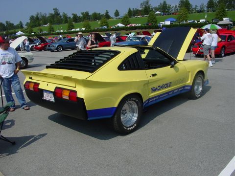 1986 Ford Mustang - A yellow custom coupe is parked at an outdoor car show with other vehicles and spectators.