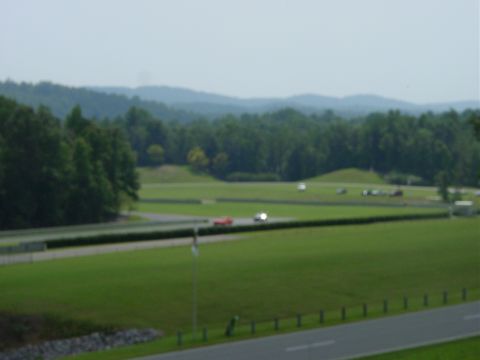 1986 Ford Mustang - A red car is seen on a race track during an event, with other vehicles visible in the background.