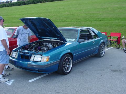 1986 Ford Mustang - A teal 1986 Ford Mustang is displayed with its hood up at an outdoor car event.