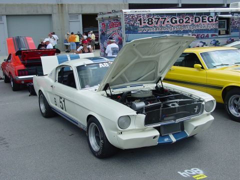 1986 Ford Mustang - A white 1965 Ford Mustang with racing stripes and an open hood is parked next to a yellow car.