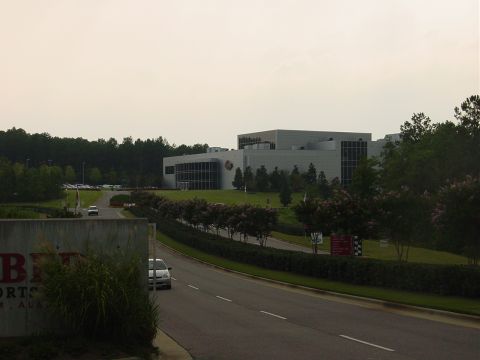 1986 Ford Mustang - A concrete sign with partial text stands in front of a modern building complex with trees lining the road.