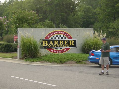 1986 Ford Mustang - A blue car is parked near the Barber Vintage Motorsports Museum sign.