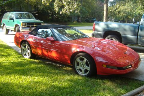 1994 Chevrolet Corvette - Red 1994 Chevrolet Corvette convertible with black top, parked outdoors near other vehicles.