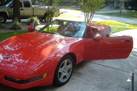 1994 Chevrolet Corvette - The red sports car's doors are open, revealing its interior, while a pickup truck sits in the background.