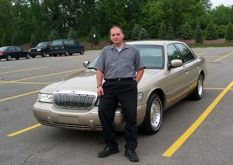1999 Mercury Marquis - A man poses with a gold sedan, possibly a Mercury Grand Marquis, in a parking lot with other vehicles visible.