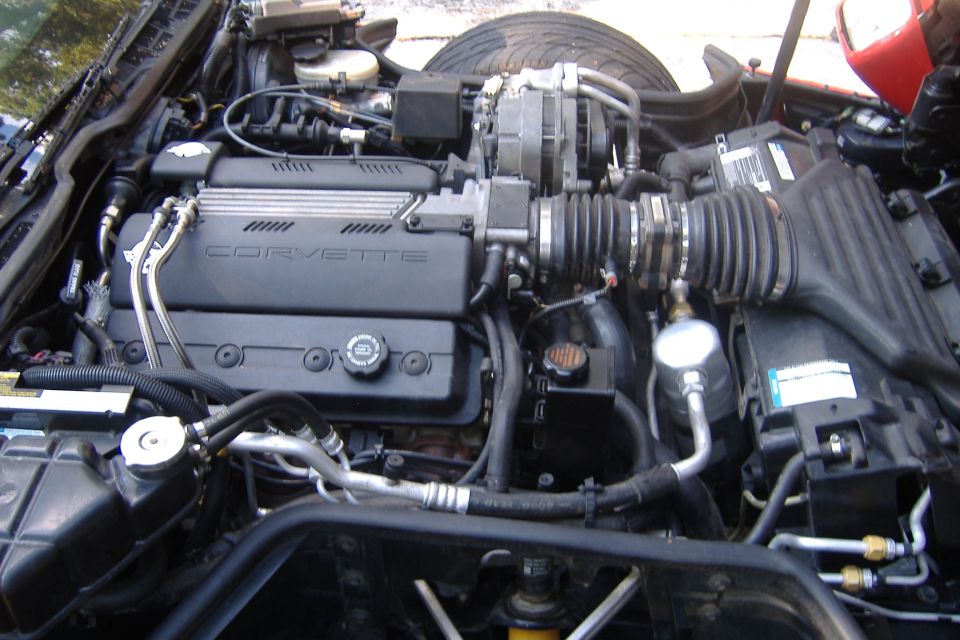 1994 Chevrolet Corvette engine bay with V8 engine, air intake, and hoses visible. 'CORVETTE' is written on the engine cover