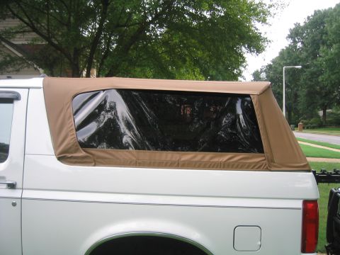 1996 Ford Bronco - Close side view of a tan soft-top rear canopy fitted to a white full-size Ford SUV in place of the factory hardtop, showing the tinted plas…